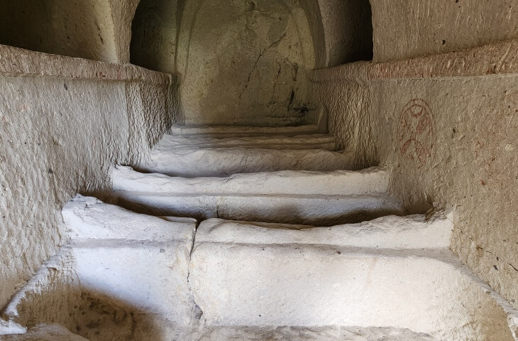 Göreme Açık Hava Müzesi’nde yer alan kaya oyma mezar odası; ölü gömme alanları basamak şeklinde sıralanmış. Sağ duvarda kırmızı haç işareti bulunuyor.